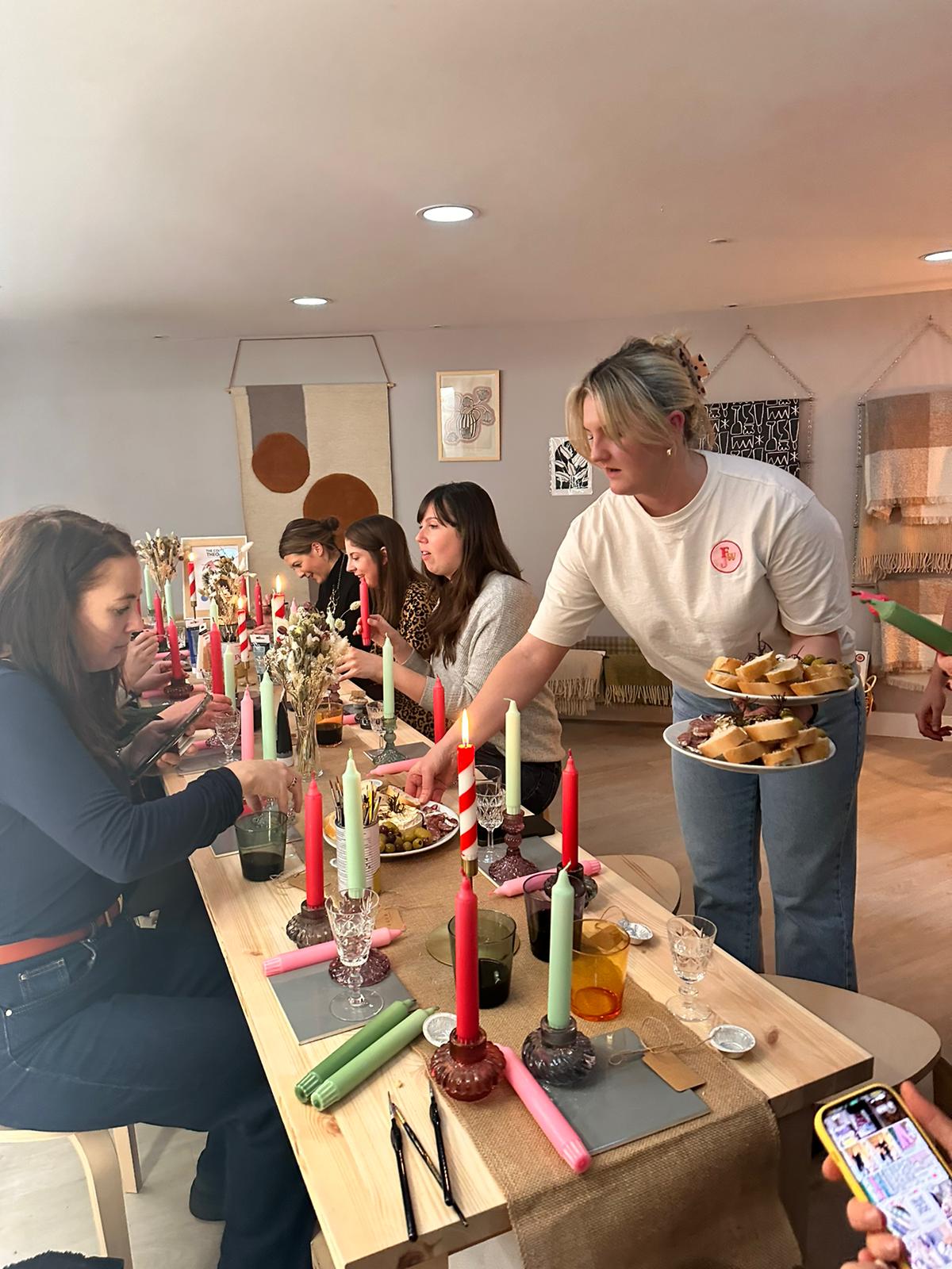 Person serving food at a table with a lot of colourful taper candles.  Other people drinking