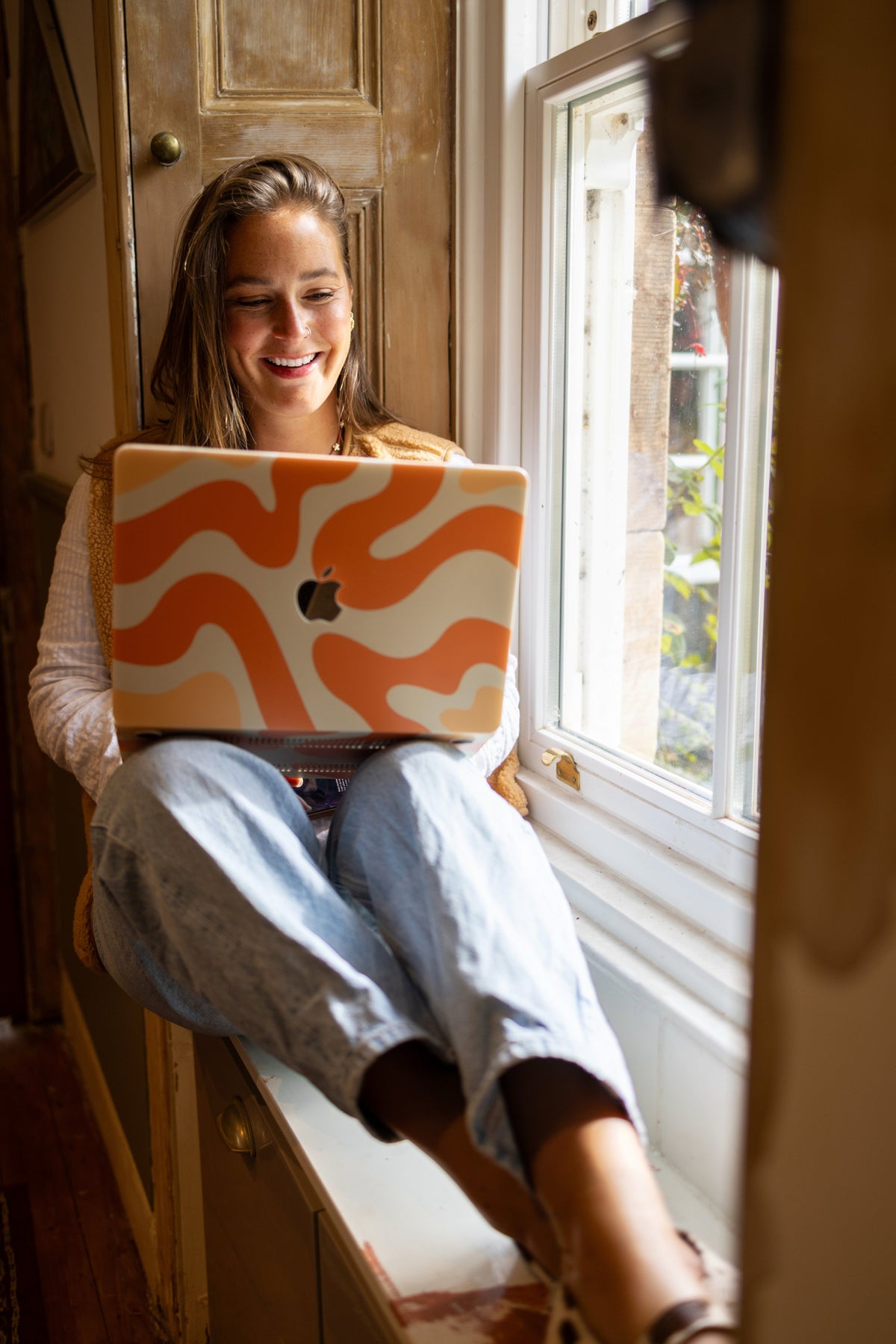 Woman using a laptop with an orange and white design in a sunlit room.