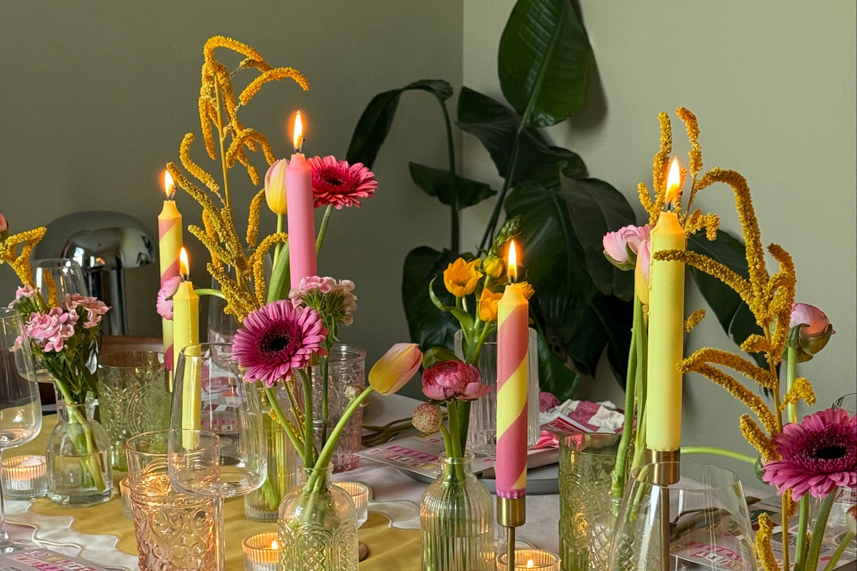 a colourful table setting, with lemon yellow and lemon yellow and pink candy striped candles, with other floral arrangements in glass vases